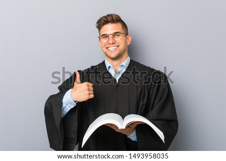 Young jurist holding a book smiling and raising thumb up