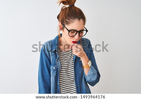 Redhead woman wearing striped t-shirt denim shirt and glasses over isolated white background feeling unwell and coughing as symptom for cold or bronchitis. Healthcare concept.