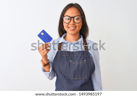 Chinese shopkeeper woman wearing glasses holding credit card over isolated white background with a happy face standing and smiling with a confident smile showing teeth