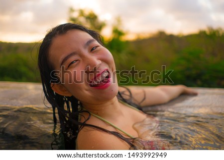 young beautiful and happy Asian Korean woman in bikini enjoying sunset taking selfie at amazing jungle resort infinity pool swimming relaxed in Summer holiday tropical destination concept