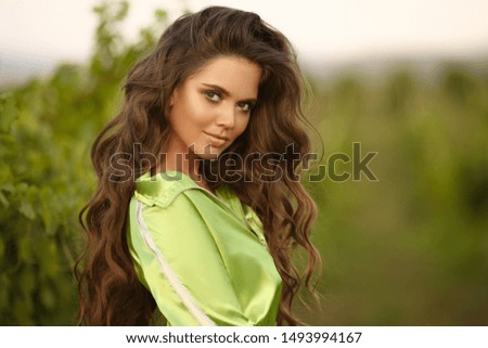 Long wavy hair. Beautiful brunette outdoor portrait. Attrctive young woman with curly hairstyle and beauty makeup posing in green vineyard. Royalty-Free Stock Photo #1493994167