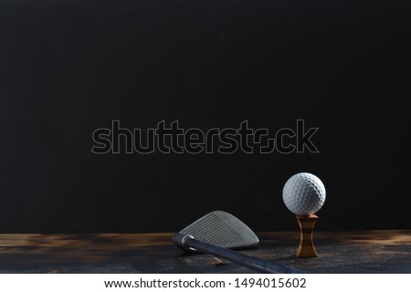 A golf ball on a tee next to a golf club in front of a black background