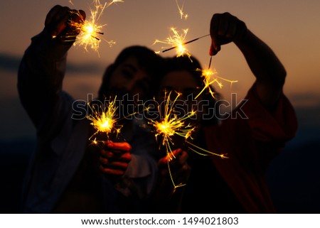 Party, event and holiday concept - man and woman fooling around with sparklers against sunset sky, low key, dark image