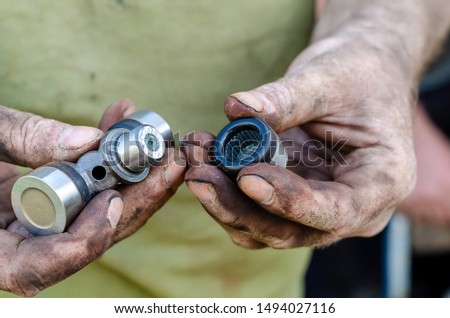 The car mechanic inspects and lubricates the new needle bearings of the universal joint shaft before installing it on the car. Eye level shooting. The horizontal version of the picture.