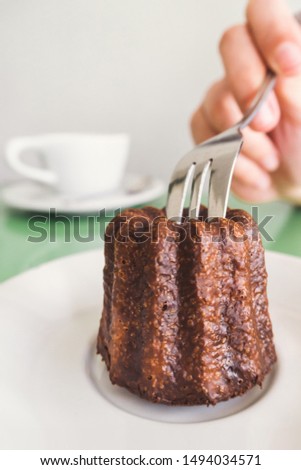 traveler woman hand holding a fork and cutting a Canelé (Canele - Caneles de bordeaux) traditional French sweet dessert bakery with white coffee cup background in coffee shop in Paris. food and lifest