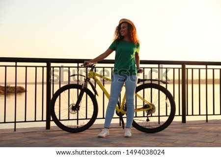 Beautiful young African-American woman with bicycle on city waterfront at sunset