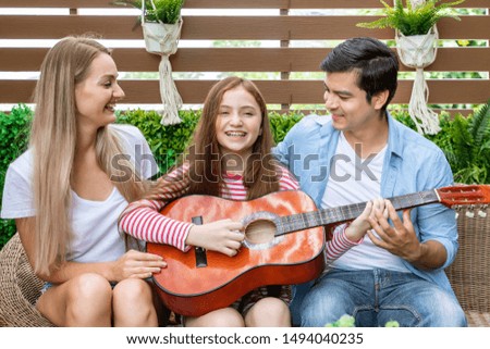 Happy family singing, and enjoy music in garden at house. Dad teaching daughter to play guitar,  family relationship concept.