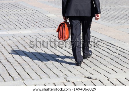 Man in a business suit carrying leather briefcase walking on the street, back view. Concept of official, businessman, politician, career advancement