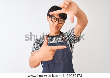 Chinese bartender man wearing apron and glasses standing over isolated white background smiling making frame with hands and fingers with happy face. Creativity and photography concept.