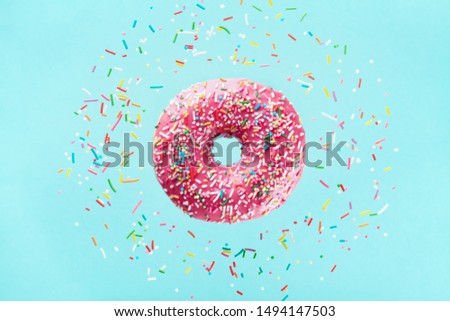 Flying sprinkled pink donut. Sweet doughnut on pastel blue background.