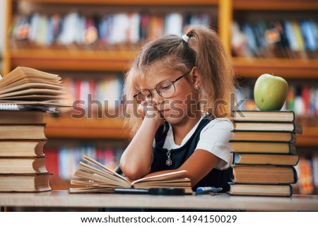 Cute little girl with pigtails is in the library. Apple on the books.