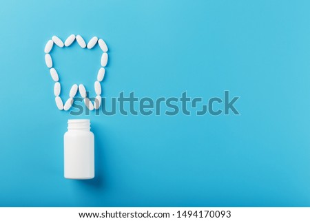Tooth made of white vitamins with calcium on a blue background. Vitamins spilled out of a tooth-shaped jar. Ca, D3.