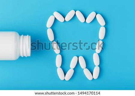 Tooth made of white vitamins with calcium on a blue background. Vitamins spilled out of a tooth-shaped jar. Ca, D3.