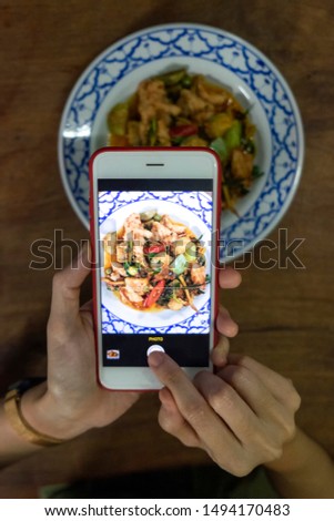 Hand holding smart phone and take a photo food on wood table. Person take a picture of food by smart phone camera. Blogger or reviewer lifestye concept.