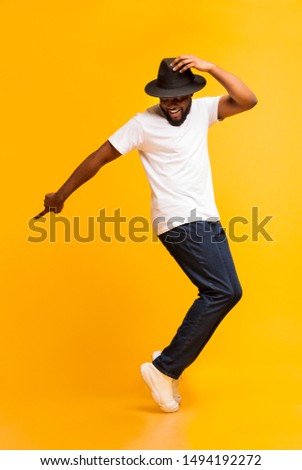 Cheerful african man dancing on tiptoes, copy michael jackson style on yellow studio background