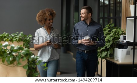 Two diverse professional colleagues talking walking in modern office, happy friendly african female and caucasian male coworkers having conversation discuss project going along business work space Royalty-Free Stock Photo #1494209714