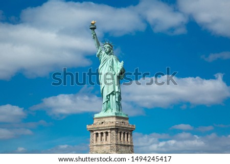 image of the statue of liberty on ellis island, behind it a beautiful blue sky with white clouds