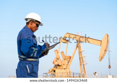 Field engineer monitoring crude oil pump in the oilfield.  Royalty-Free Stock Photo #1494263468