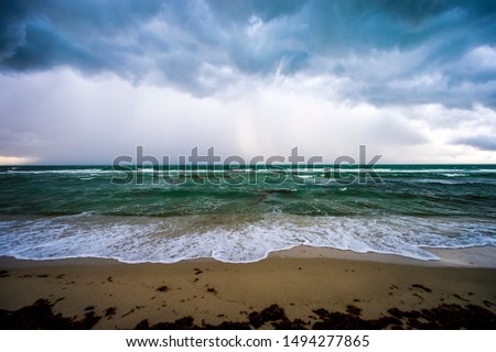 Dramatic stormy weather view of tropical waves with an infestation of brown sargassum seaweed washing ashore under a dark rain squall