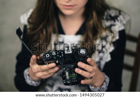 Young girl with a vintage camera opens film compartment and looks at a film frames. She adjusts the camera. Woman sets old camera for work. Girl in school uniform checks the photos created