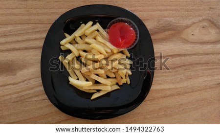 French fries on a black plate with tomato sauce on a wooden background. ( Top View )