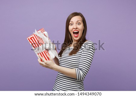 Young brunette woman girl in casual striped clothes posing isolated on violet purple background studio portrait. People sincere emotions lifestyle concept. Mock up copy space. Hold gift present box