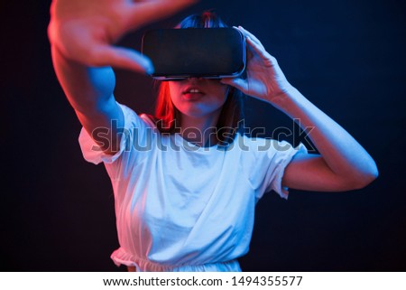 It's quite interesting. Young woman using virtual reality glasses in the dark room with neon lighting.