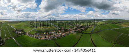 Dramatic aerial panoramic view of the agrarian green pasture fields with its irrigation infrastructure of ditches and trenches surrounding the small traditional village of Ransdorp near Amsterdam