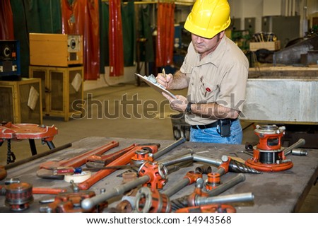 Auditor taking inventory of tools in an industrial factory.  Welding equipment is visible in the background.