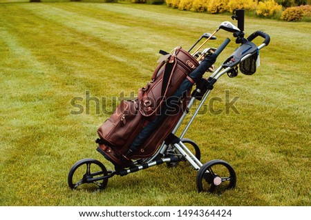 Leather stylish brown bag with golf clubs on a special cart on the golf course.