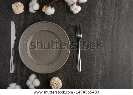 Empty gray dish with knife and fork on a slate background with a cotton branch, with copy space for your menu or recipe. Menu card for restaurants and table setting. Horizontal photo. Flat lay