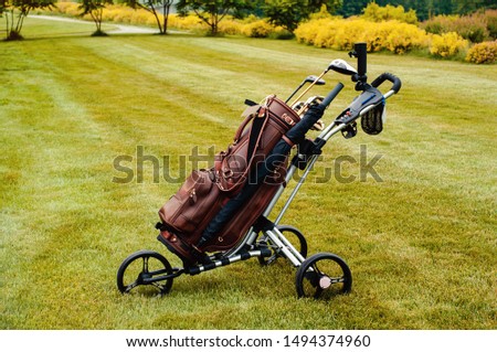 Leather stylish brown bag with golf clubs on a special cart on the golf course.