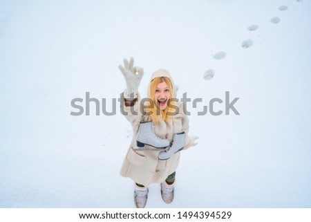 Funny face. Beautiful happy laughing young woman wearing winter hat gloves and scarf covered with snow flakes. Winter woman portrait outdoor