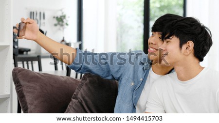 Two young asian men friend taking photo together, asia gay couple selfie with phone while sitting in home living room, friendship, homosexual and lgbt concept