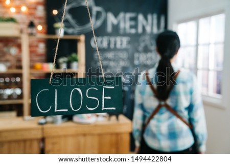 Women worker shop owner flip sign to close the shop. blackboard chalkboard door plate hanging on glass door window. blurred back view of female waitress in apron walk back to counter ready to rest.