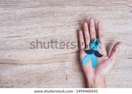 Prostate Cancer Awareness, Man holding light Blue Ribbon with mustache on wooden background for supporting people living and illness. Men Healthcare and World cancer day concept