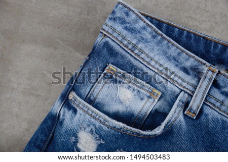 Front right pocket on blue jeans. Side view on gray background

