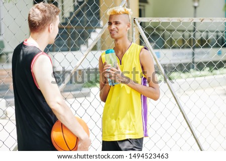 Young tall basketball players drinking water and talking during break between quarters