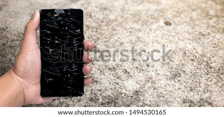 The screen of a telephone ripped in a man's hand on a cement wall background