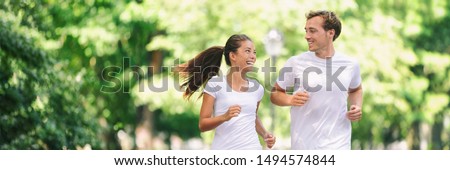 Run exercise fitness friends walking running talking together on fun race in city park panoramic banner background. Healthy active lifestyle young people, Asian woman, Caucasian man couple.