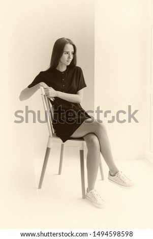 Young girl in black dress is sitting on a chair in the room
