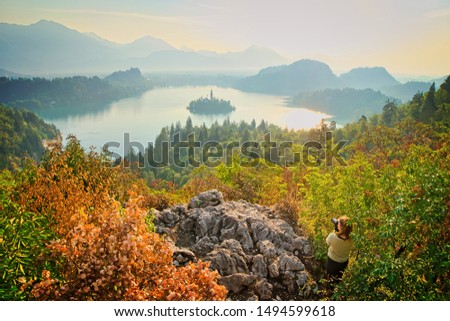 Female photographer is taking photograpgh of dramatic scenic panorama of Bled lake in Slovenia Triglav national park. Europe autumn background with colorful nature around.