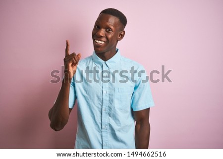 African american man wearing blue casual shirt standing over isolated pink background pointing finger up with successful idea. Exited and happy. Number one.