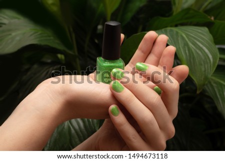 Female hand with green nail design holding nail polish bottle