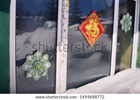 The red Chinese "blessing and Open door lucky" and snowflake patterns are attached to the glass of the outdoor window, and the outdoor snow and pine trees are reflected. the Chinese rural New Year.