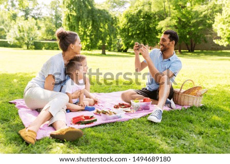 family, leisure and people concept - father taking picture of happy mother with two little sons by smartphone on picnic at summer park