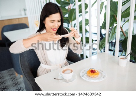 technology, leisure and people concept - happy asian woman with smartphone photographing her coffee and cake at cafe