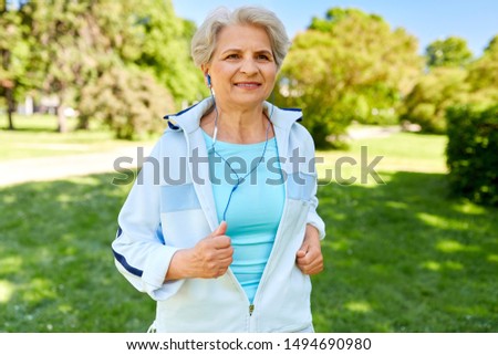 fitness, sport and healthy lifestyle concept - senior woman with earphones listening to music and running along summer park