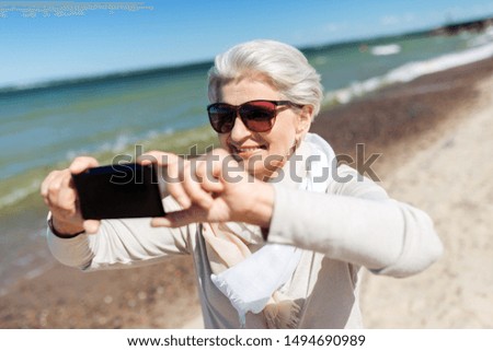 old people and leisure concept - happy smiling senior woman taking selfie by smartphone on beach in estonia