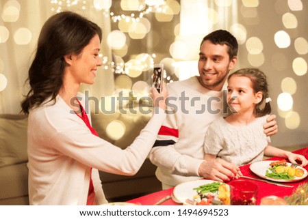 holidays, family and celebration concept - happy mother, father and little daughter having christmas dinner and taking picture by smartphone at home